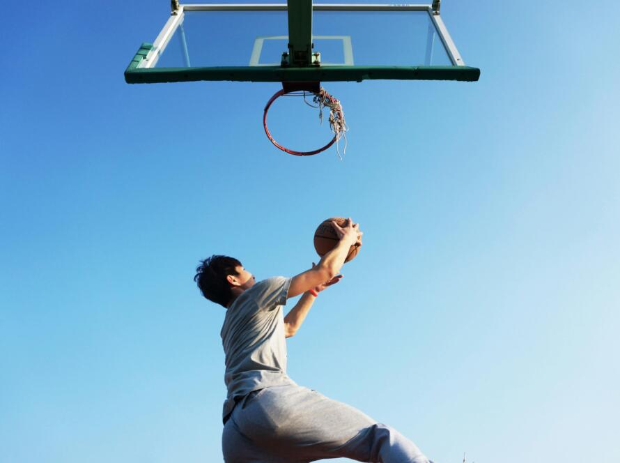 A young man jumping to dunk a basketball outdoors in clear daylight.